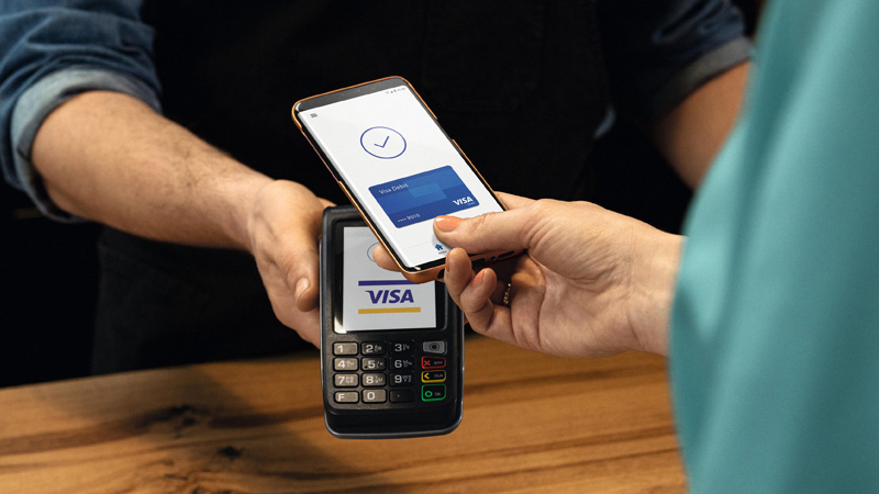 Hand taps smartphone on payment terminal to pay with Visa