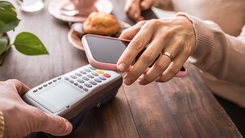 Hand hält Smartphone auf kontaktloses Terminal zum mobilen Bezahlen